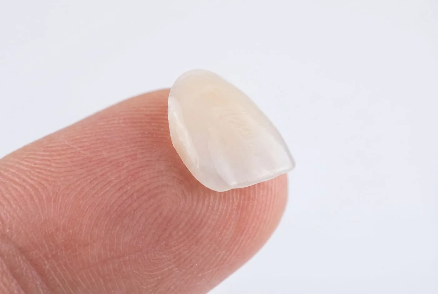 A single ultra-thin porcelain veneer resting on a fingertip showing its remarkable thinness